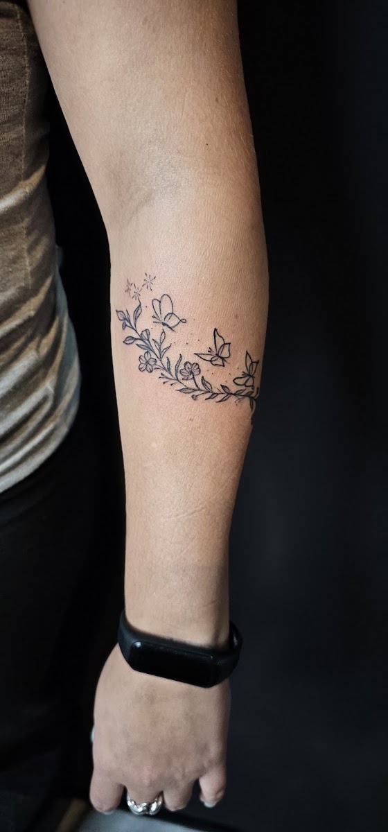 Tatuaje fineline de flores y mariposas en el antebrazo